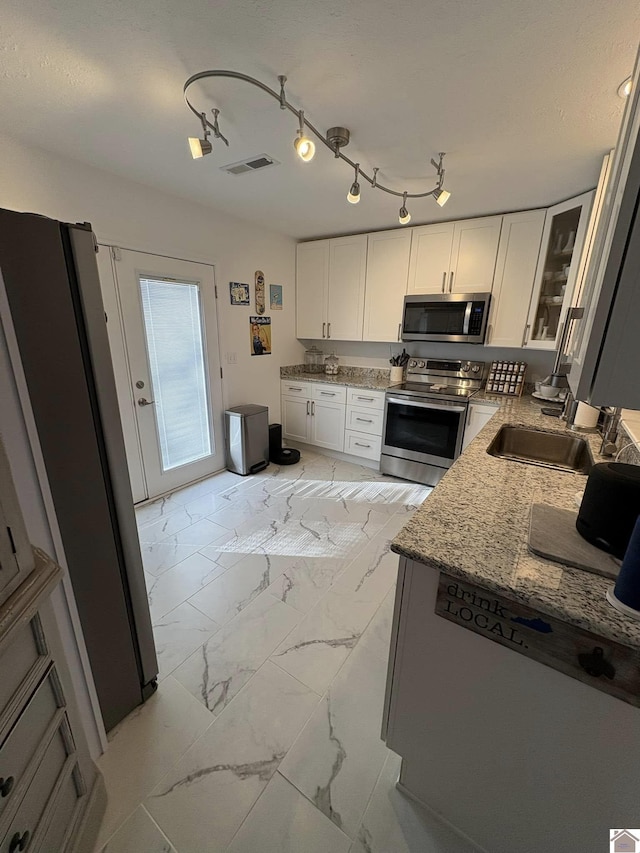 kitchen featuring white cabinets, appliances with stainless steel finishes, light stone countertops, and sink