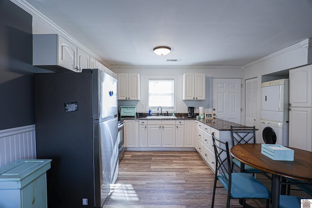 kitchen with sink, stainless steel appliances, light hardwood / wood-style flooring, stacked washer / dryer, and white cabinets