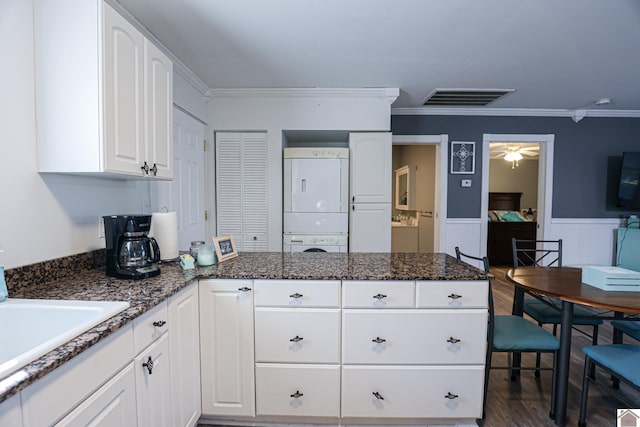 kitchen featuring dark stone counters, stacked washer and clothes dryer, crown molding, dark hardwood / wood-style flooring, and white cabinetry