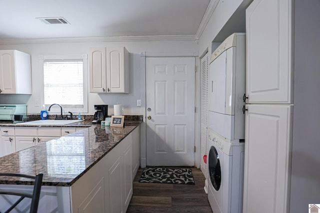 kitchen with sink, dark hardwood / wood-style flooring, dark stone countertops, stacked washer / drying machine, and white cabinets