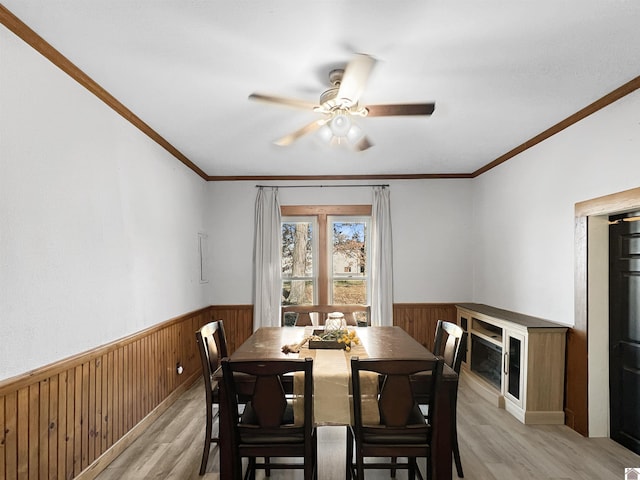 dining area with ceiling fan, wooden walls, ornamental molding, and light wood-type flooring