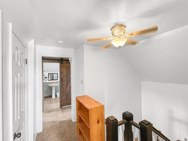 hallway featuring a textured ceiling, a barn door, light colored carpet, and vaulted ceiling