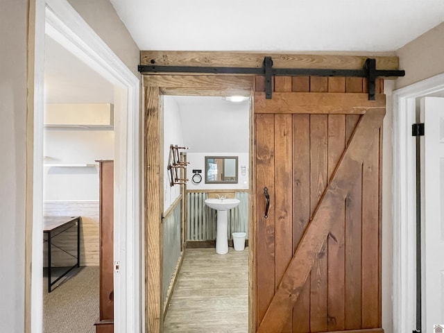 corridor featuring a barn door, light hardwood / wood-style floors, and wooden walls