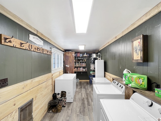 laundry room featuring light hardwood / wood-style floors, wood walls, and washing machine and clothes dryer