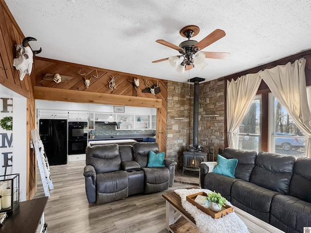 living room featuring a wood stove, wooden walls, a textured ceiling, and light wood-type flooring