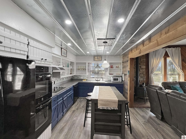 kitchen featuring black appliances, white cabinets, blue cabinets, wooden walls, and a kitchen bar