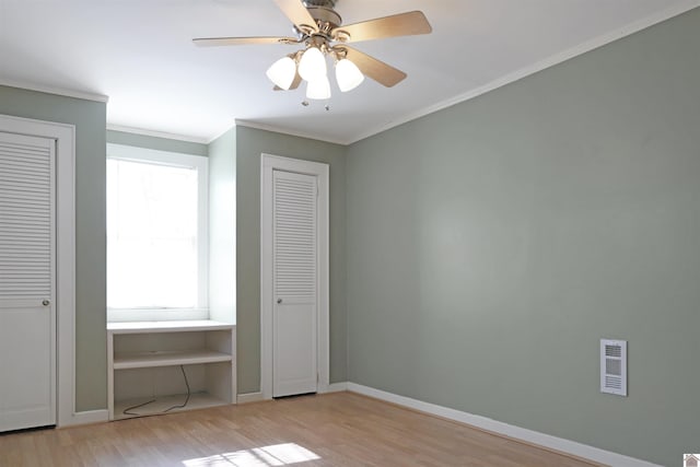 unfurnished bedroom featuring two closets, light hardwood / wood-style flooring, ceiling fan, and crown molding