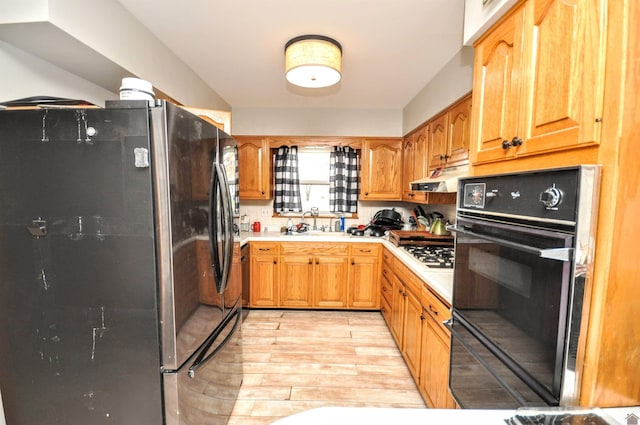 kitchen with sink, stainless steel fridge, black oven, light hardwood / wood-style floors, and gas cooktop