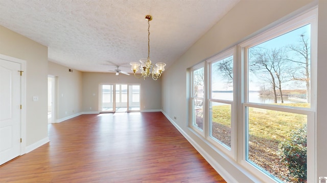 unfurnished dining area with ceiling fan with notable chandelier, wood-type flooring, a textured ceiling, and a water view