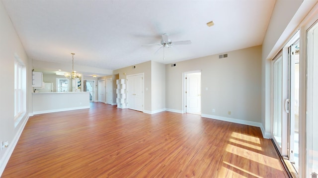 unfurnished living room featuring ceiling fan with notable chandelier and light wood-type flooring