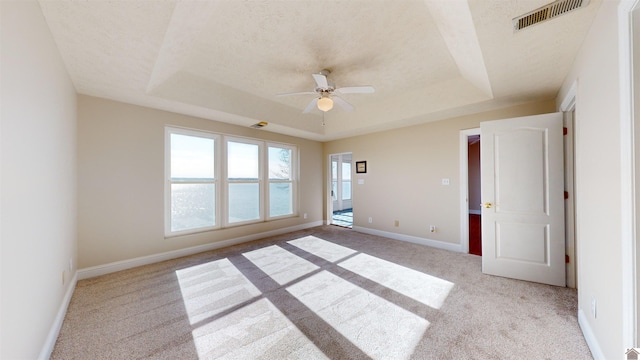 empty room with ceiling fan, light colored carpet, a textured ceiling, a tray ceiling, and a water view