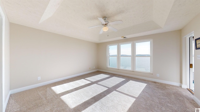 carpeted empty room featuring a textured ceiling, a water view, a raised ceiling, and ceiling fan