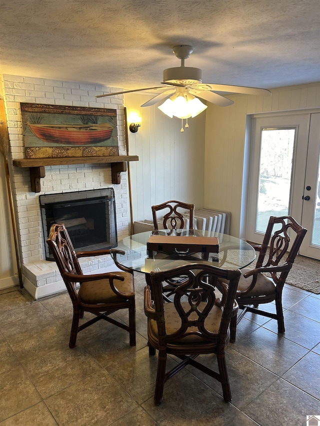 tiled dining room with a fireplace, a textured ceiling, ceiling fan, and wooden walls