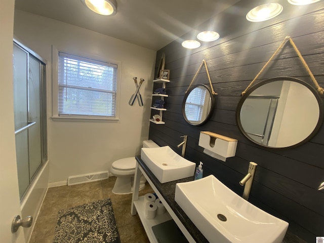 full bathroom featuring wood walls, sink, combined bath / shower with glass door, and toilet