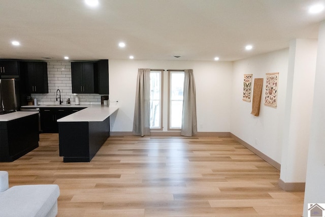 kitchen featuring kitchen peninsula, tasteful backsplash, sink, light hardwood / wood-style flooring, and stainless steel refrigerator