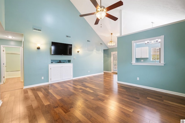 unfurnished living room featuring ceiling fan with notable chandelier, dark wood-type flooring, and high vaulted ceiling