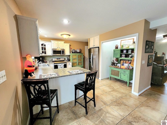 kitchen featuring white cabinetry, a kitchen bar, kitchen peninsula, and appliances with stainless steel finishes