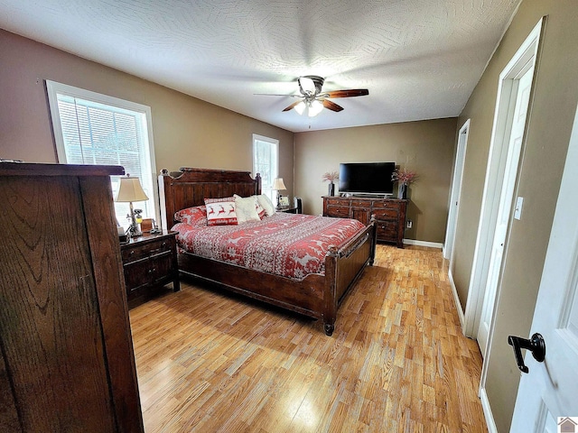 bedroom with ceiling fan, light hardwood / wood-style floors, a textured ceiling, and multiple windows