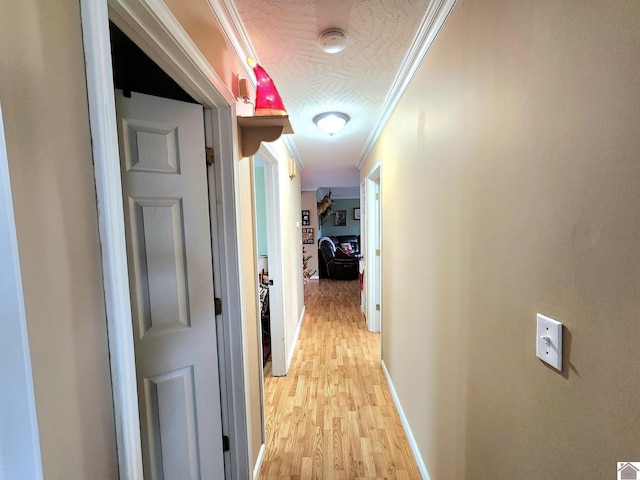 hallway with ornamental molding, a textured ceiling, and light hardwood / wood-style flooring