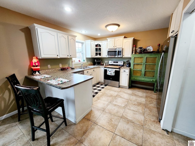 kitchen featuring sink, kitchen peninsula, a breakfast bar area, white cabinetry, and stainless steel appliances