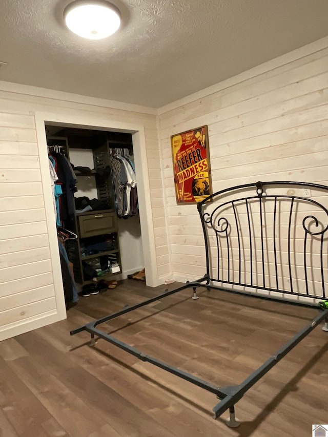 bedroom with wood walls, a closet, dark wood-type flooring, and a textured ceiling