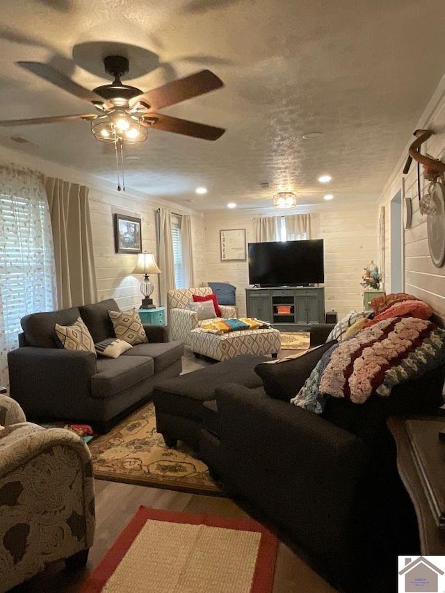 living room with ceiling fan, wooden walls, wood-type flooring, and a textured ceiling