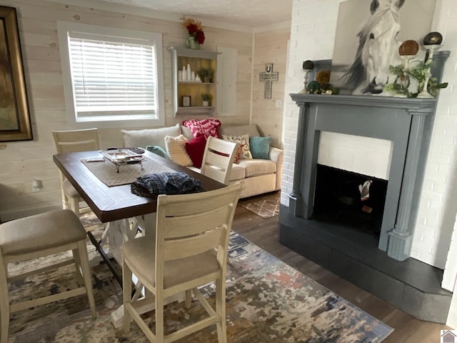 dining space with hardwood / wood-style flooring, wooden walls, and a brick fireplace