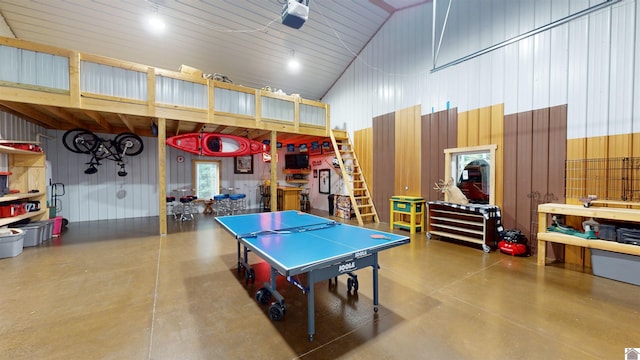 playroom featuring wooden walls, high vaulted ceiling, and concrete floors