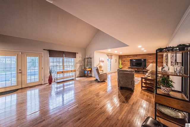 living room featuring lofted ceiling, light wood-type flooring, ornamental molding, and french doors