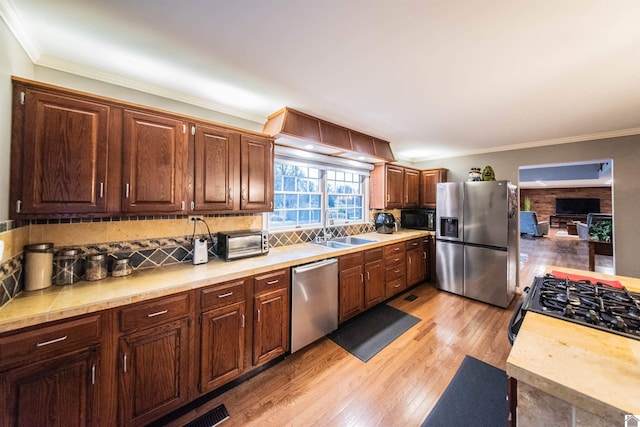 kitchen featuring light wood-type flooring, sink, appliances with stainless steel finishes, and ornamental molding