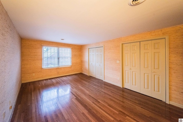 unfurnished bedroom with dark wood-type flooring and two closets