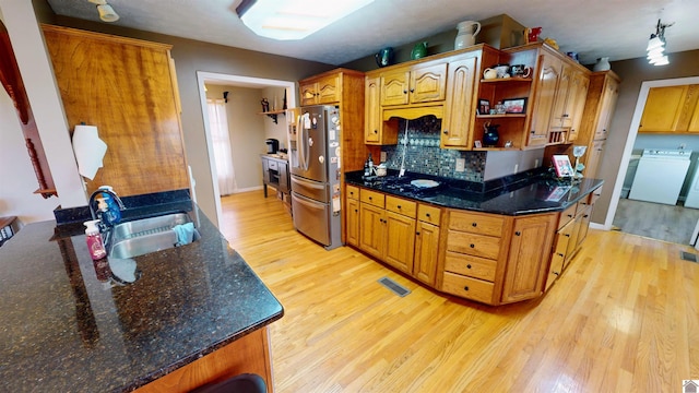 kitchen with backsplash, sink, light hardwood / wood-style flooring, washer / dryer, and stainless steel refrigerator