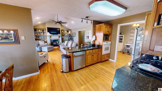 kitchen featuring stainless steel appliances, vaulted ceiling, ceiling fan, sink, and light hardwood / wood-style flooring