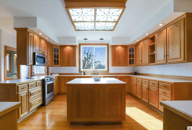 kitchen featuring sink, appliances with stainless steel finishes, pendant lighting, a kitchen island, and light wood-type flooring