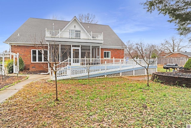 rear view of house featuring a balcony, a wooden deck, a lawn, and a sunroom