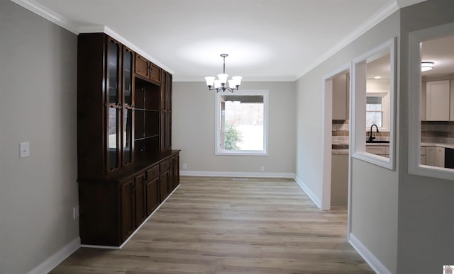 unfurnished dining area with light wood-type flooring, ornamental molding, a chandelier, and sink