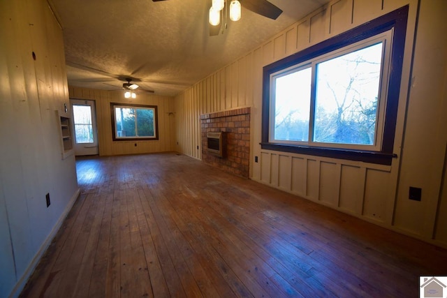 unfurnished living room featuring wood-type flooring, a textured ceiling, a brick fireplace, and ceiling fan