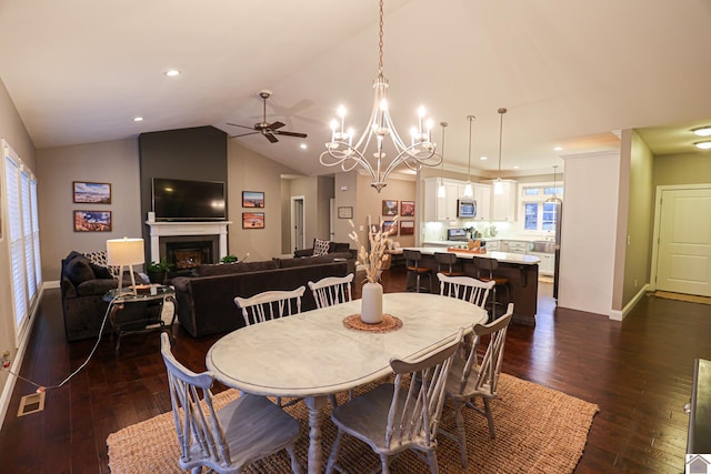 dining space with a fireplace, ceiling fan with notable chandelier, dark hardwood / wood-style floors, and lofted ceiling