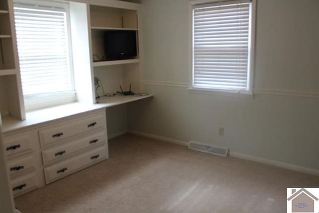 interior space featuring light colored carpet, built in desk, and multiple windows