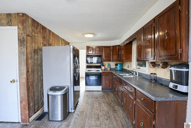 kitchen with wood walls, white range with electric cooktop, sink, stainless steel refrigerator with ice dispenser, and a textured ceiling