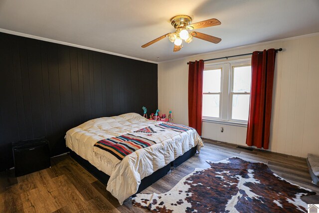 bedroom with ceiling fan, crown molding, wood walls, and dark hardwood / wood-style floors