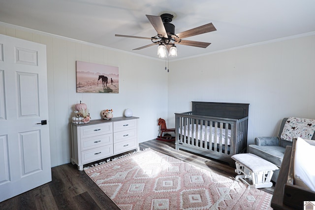 bedroom featuring ceiling fan, a crib, ornamental molding, and dark wood-type flooring