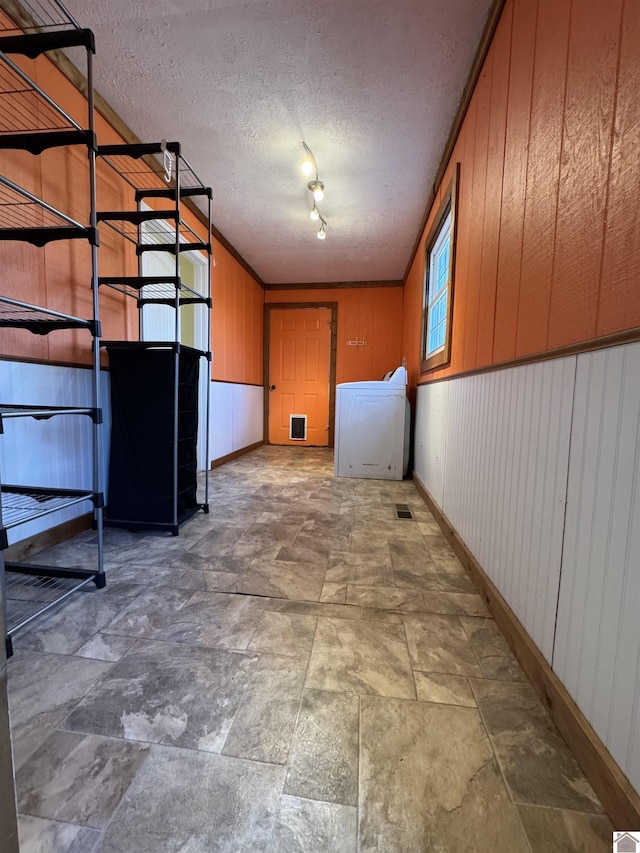 basement featuring a textured ceiling, wood walls, and rail lighting