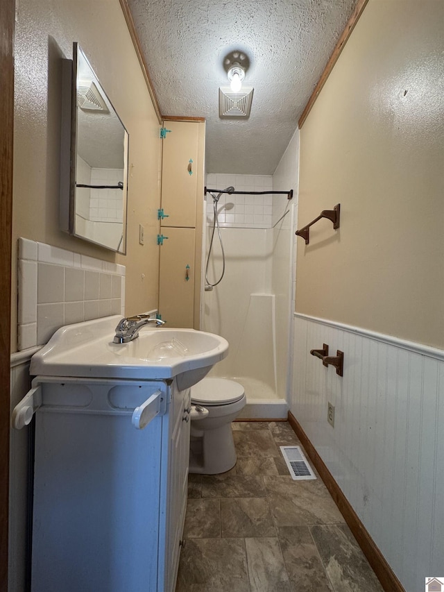 bathroom with a shower, vanity, a textured ceiling, and toilet