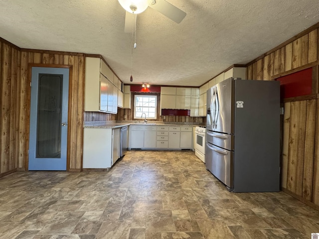 kitchen with appliances with stainless steel finishes, ceiling fan, wooden walls, crown molding, and white cabinetry