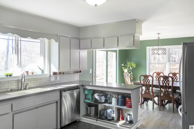 kitchen with kitchen peninsula, tasteful backsplash, stainless steel appliances, sink, and decorative light fixtures