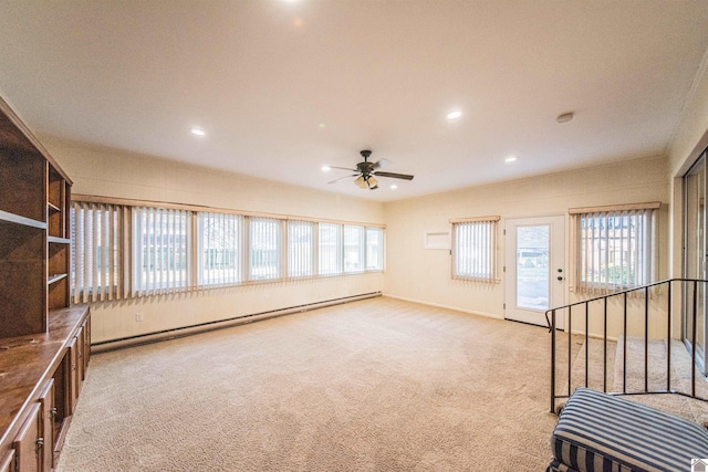 unfurnished living room featuring light colored carpet, a wealth of natural light, a baseboard heating unit, and ceiling fan