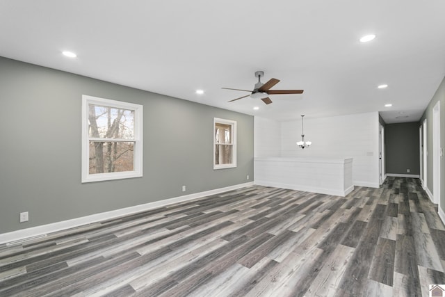 unfurnished living room featuring ceiling fan with notable chandelier and dark hardwood / wood-style floors