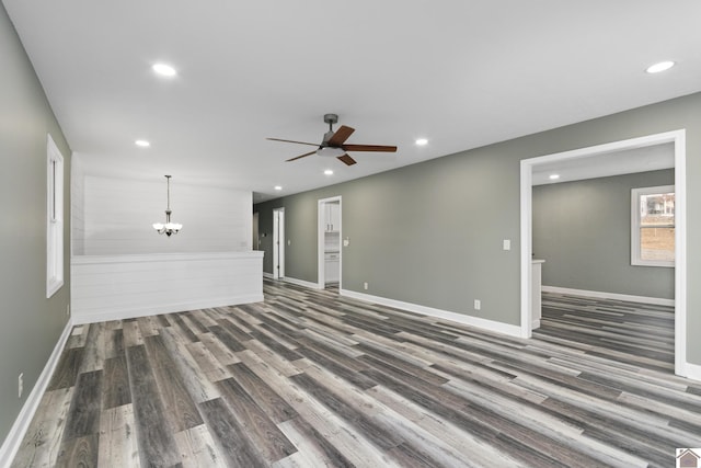 unfurnished living room featuring ceiling fan with notable chandelier and dark wood-type flooring