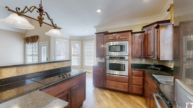 kitchen featuring appliances with stainless steel finishes, sink, decorative light fixtures, dark stone countertops, and light hardwood / wood-style floors